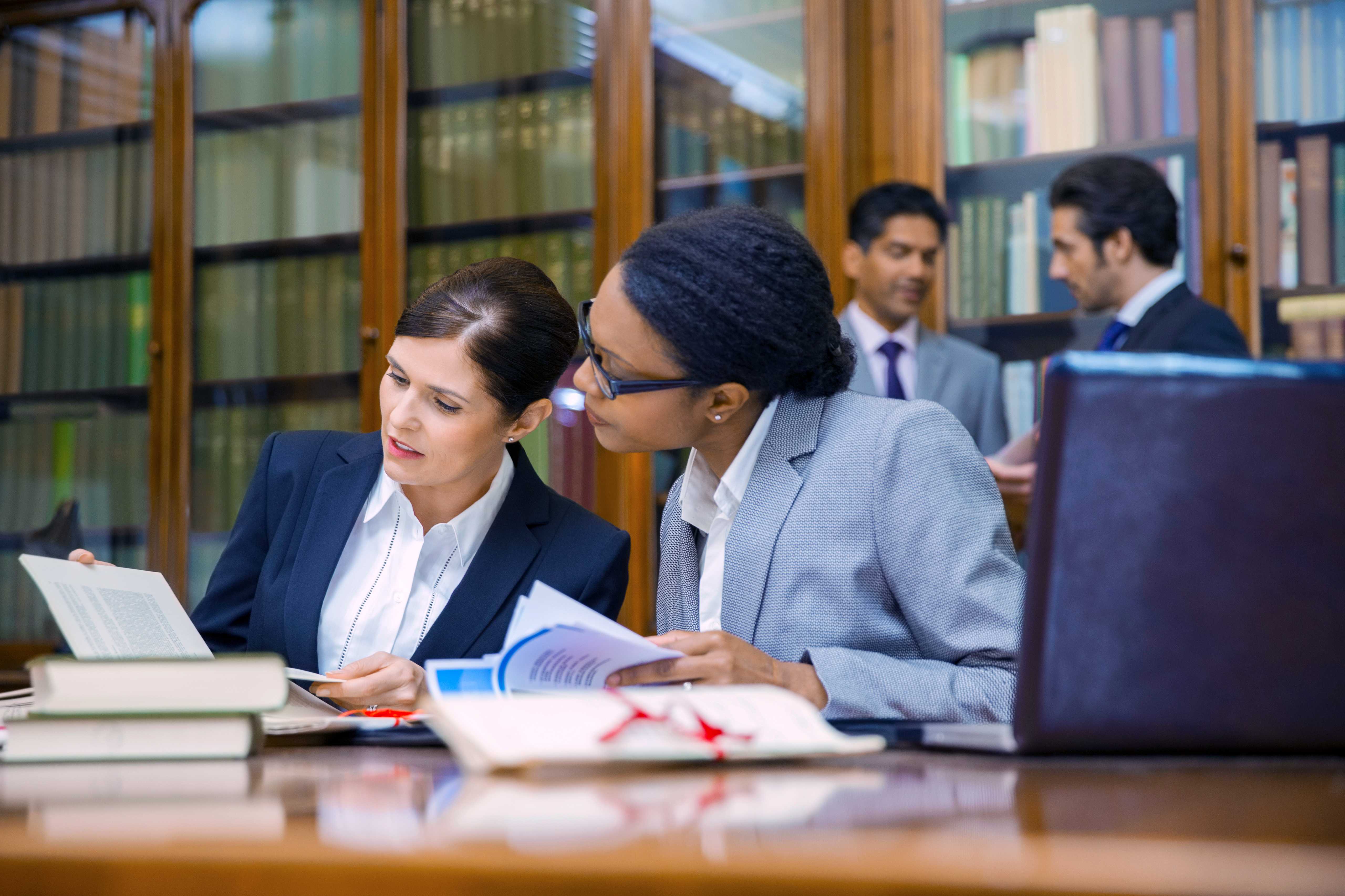 Several law professionals examine books and other documents in a law library.